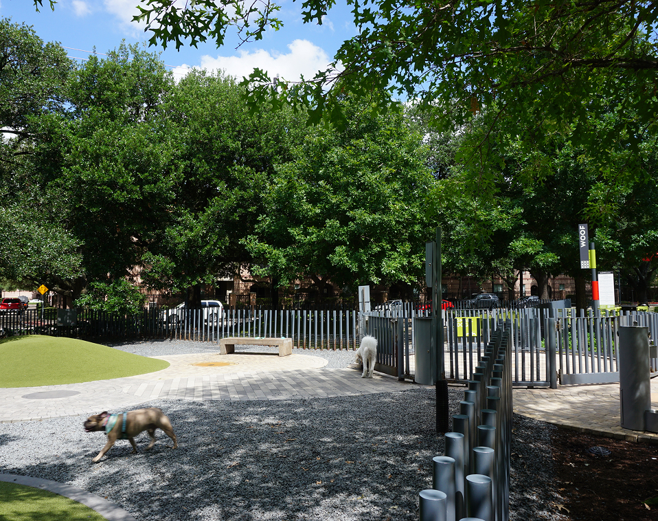 Playground area at Levy Park featuring a custom fabricated metal fence with shaded green spaces and recreational equipment in the background