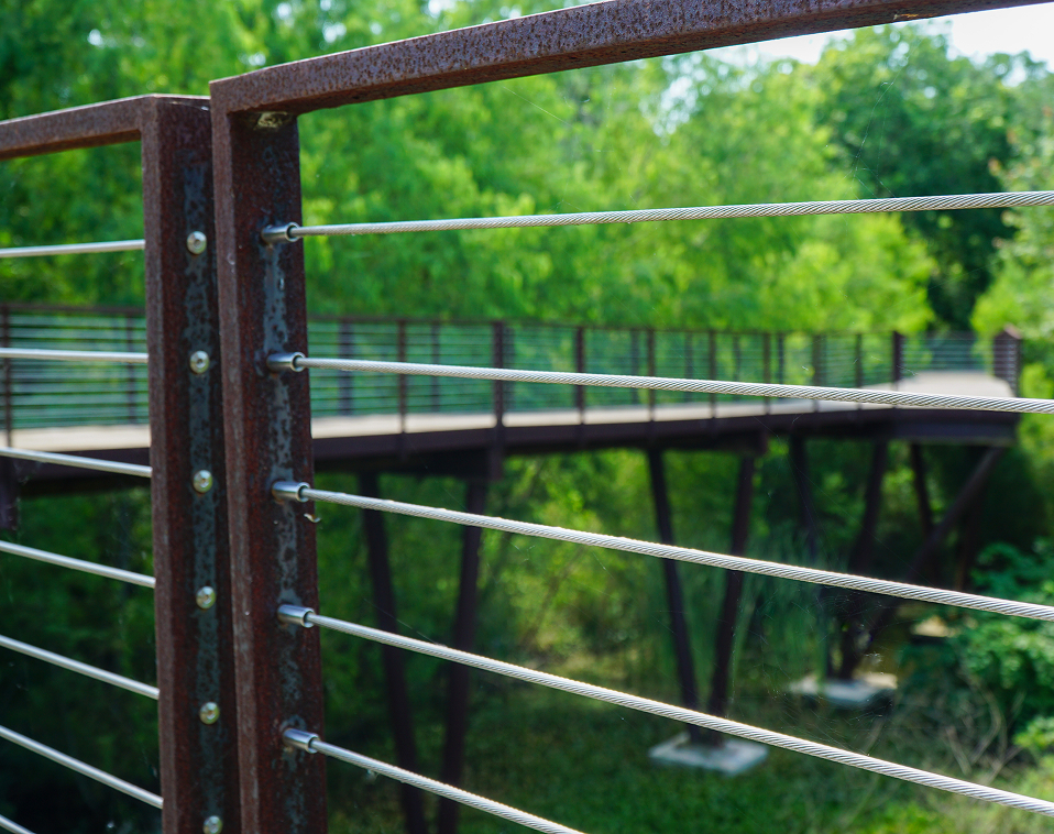 Close-up of weathered steel railing with cable rail design by Renfrow+Co, framing the elevated wooden walkway of the High Island Sky Walk