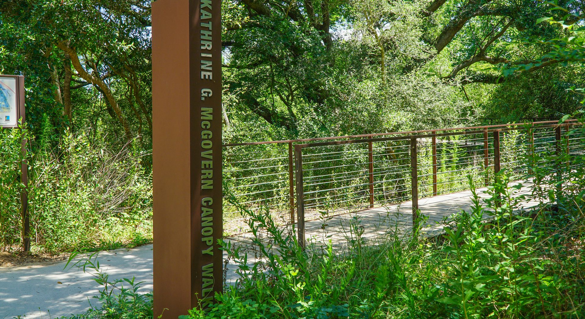 Kathrine G. McGovern Canopy Walk entrance with a metal signpost and cable-railed elevated walkway surrounded by dense greenery