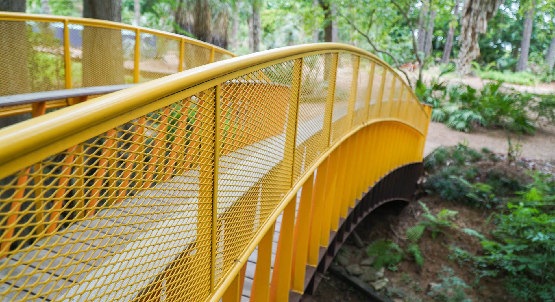 Renfrow+Co expertly fabricated this bridge railing, featuring a striking combination of yellow stainless steel mesh and a sturdy Ipe wood walkway, in John Fairey Garden